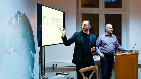 Two men holding a presentation; one standing next to the computer and the other one explaining something on the screen